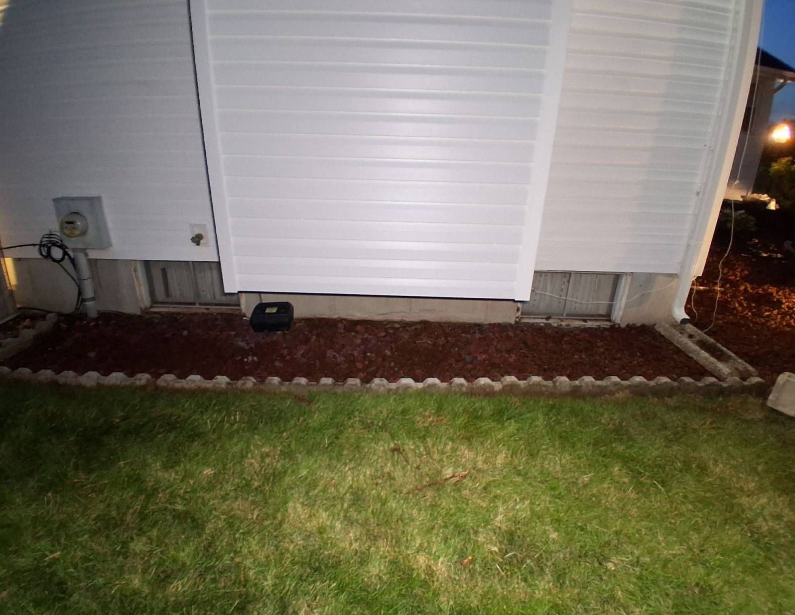 A white house with mulch in a bed, a gray concrete foundation, and green grass.