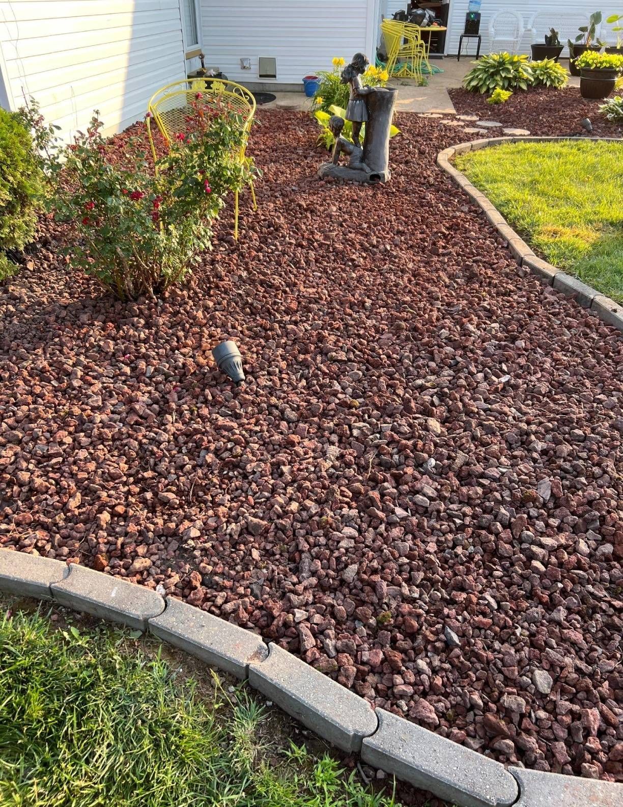 Red lava rock landscaping with stone edging, flowers, and small decorative statue.