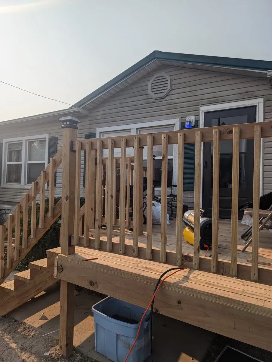 Wooden deck with stairs, railing, and siding house in background.