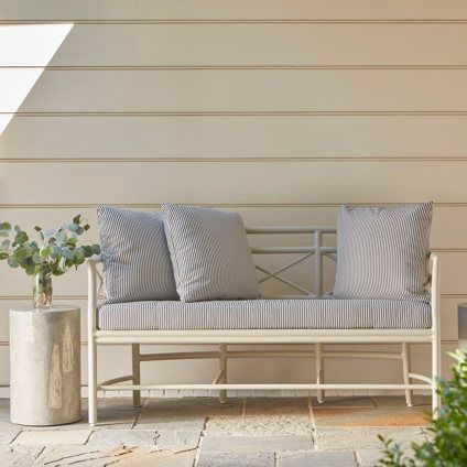 A white bench with striped pillows is sitting on a patio.