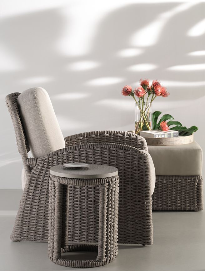 A wicker chair and ottoman with a vase of flowers on a table.