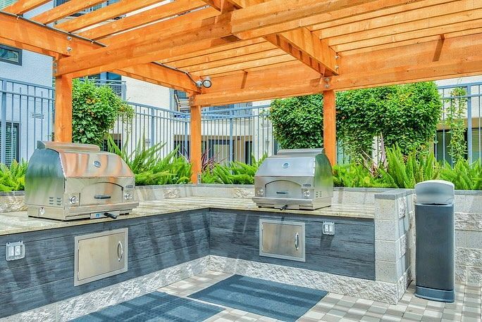 A large outdoor kitchen with two grills under a wooden pergola.