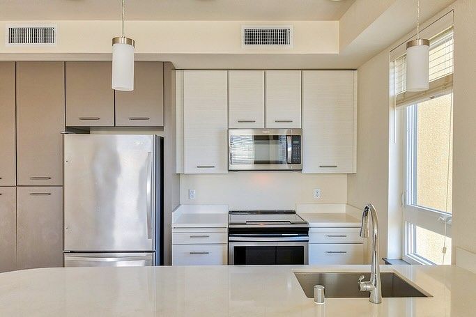 A kitchen with white cabinets , stainless steel appliances , a sink and a refrigerator.