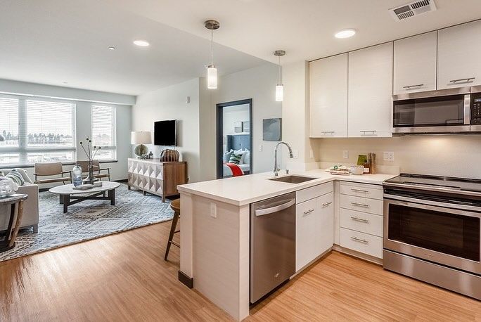 A kitchen with stainless steel appliances and white cabinets is open to a living room.