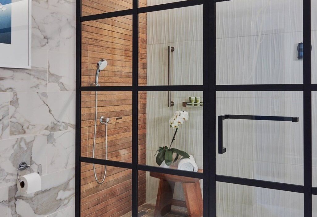 A woman is taking a shower in a bathroom with a glass shower door.