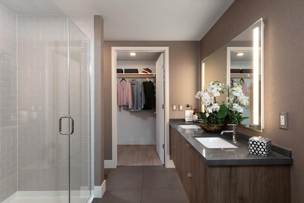 A bathroom with a walk in closet , sink , mirror and shower.