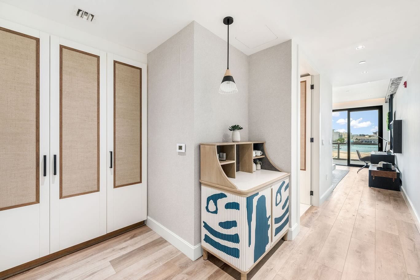 A hallway with a desk and a sliding glass door leading to a living room.