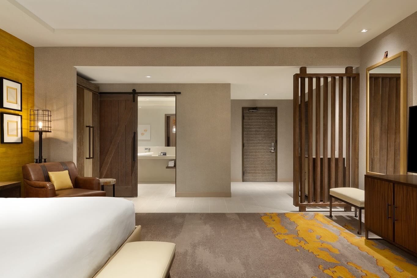 A hotel room with a king size bed , chair , dresser and television.