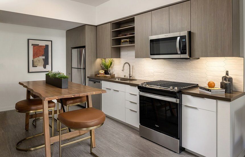 A kitchen with stainless steel appliances , wooden cabinets , a table and chairs.