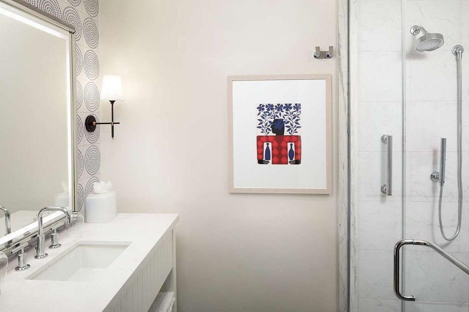 A bathroom with a sink , mirror , shower and a picture on the wall.