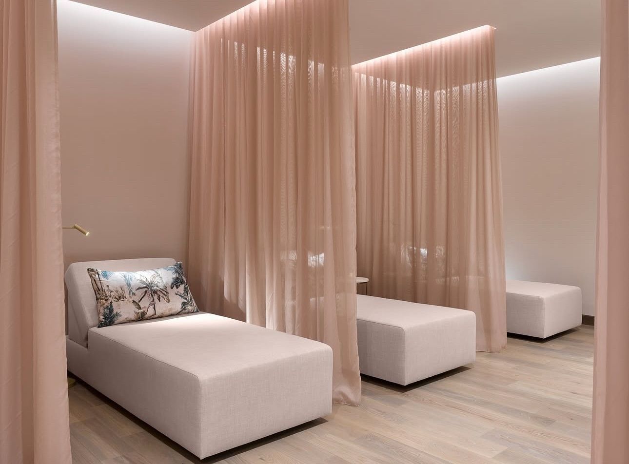 There are three beds in a room with pink curtains.