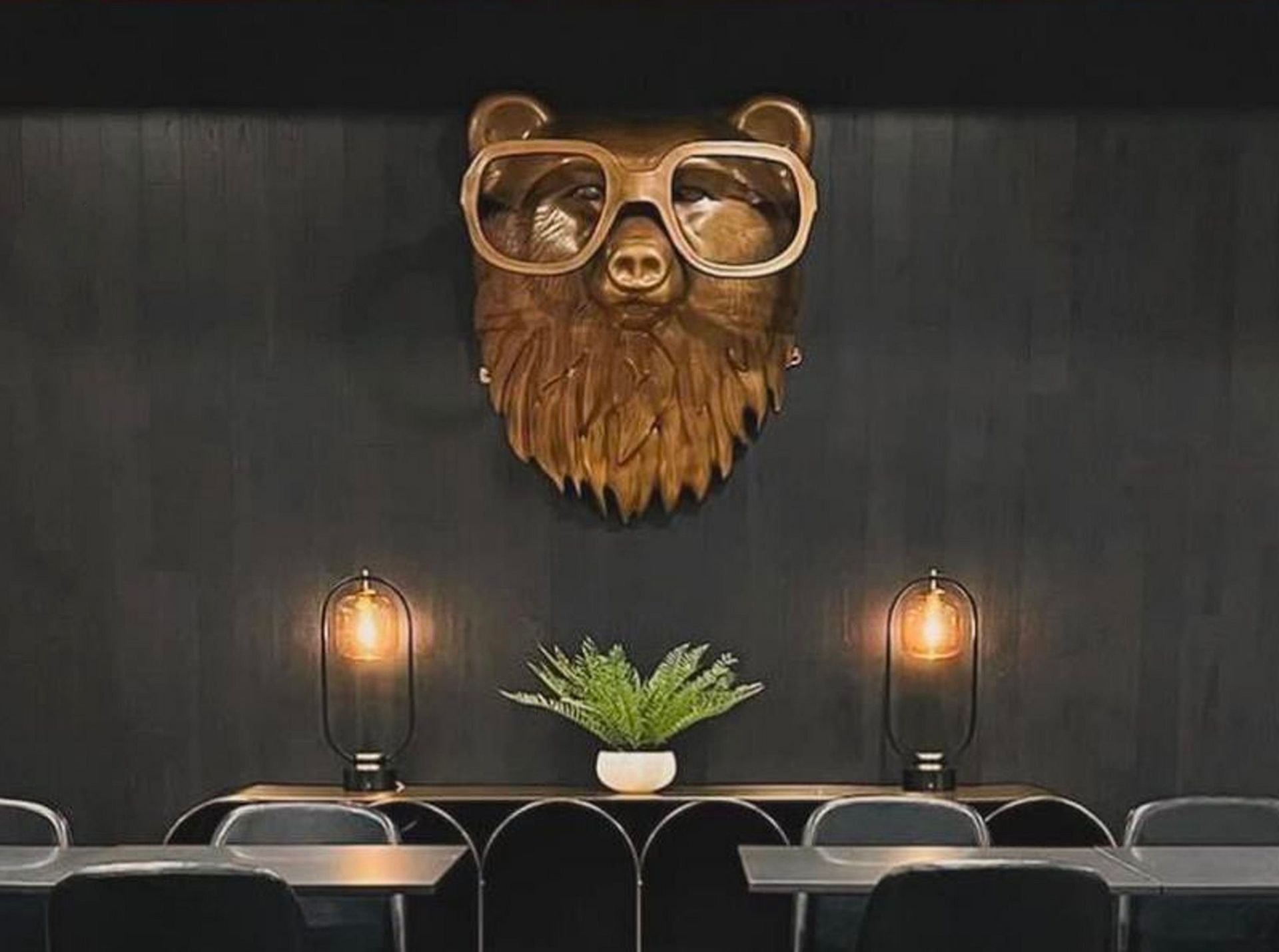 A wooden bear head with glasses and a beard is hanging on a wall.