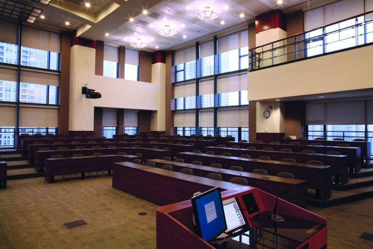 A large room with rows of tables and a podium with a laptop on it