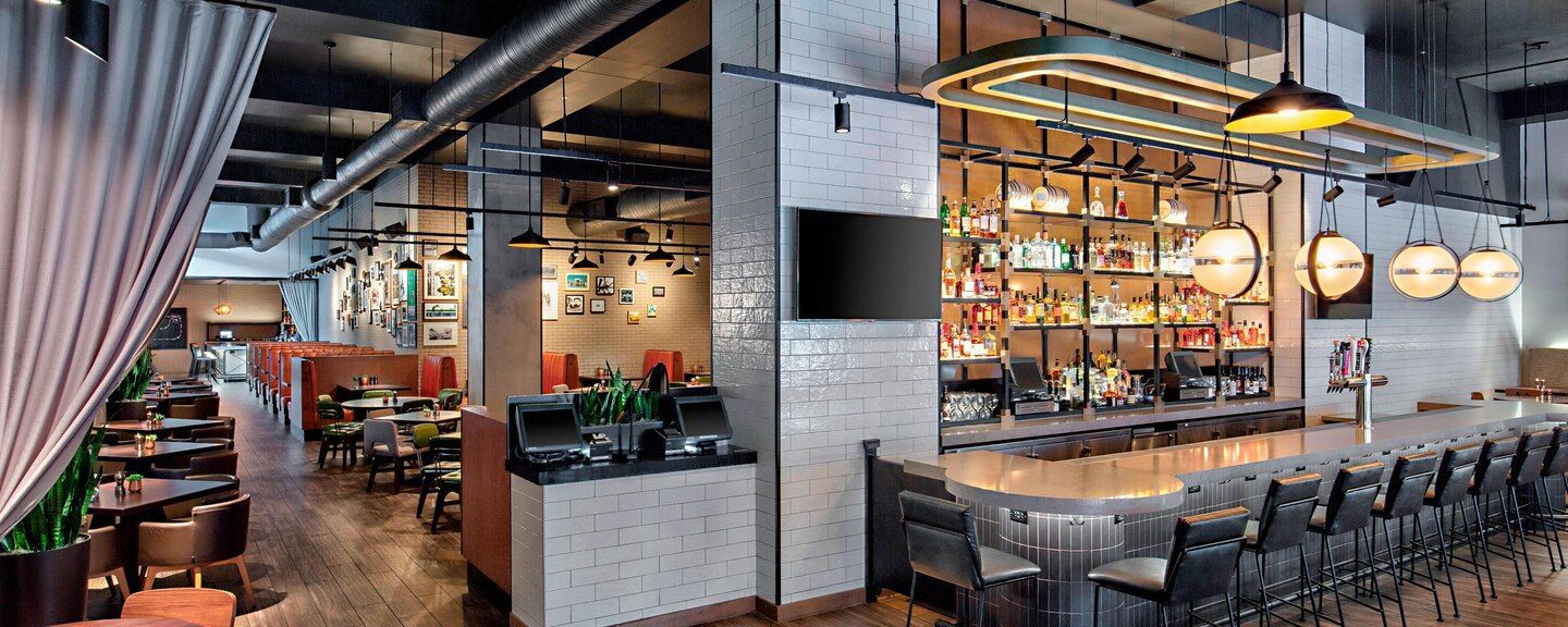 A restaurant with a long bar and tables and chairs.