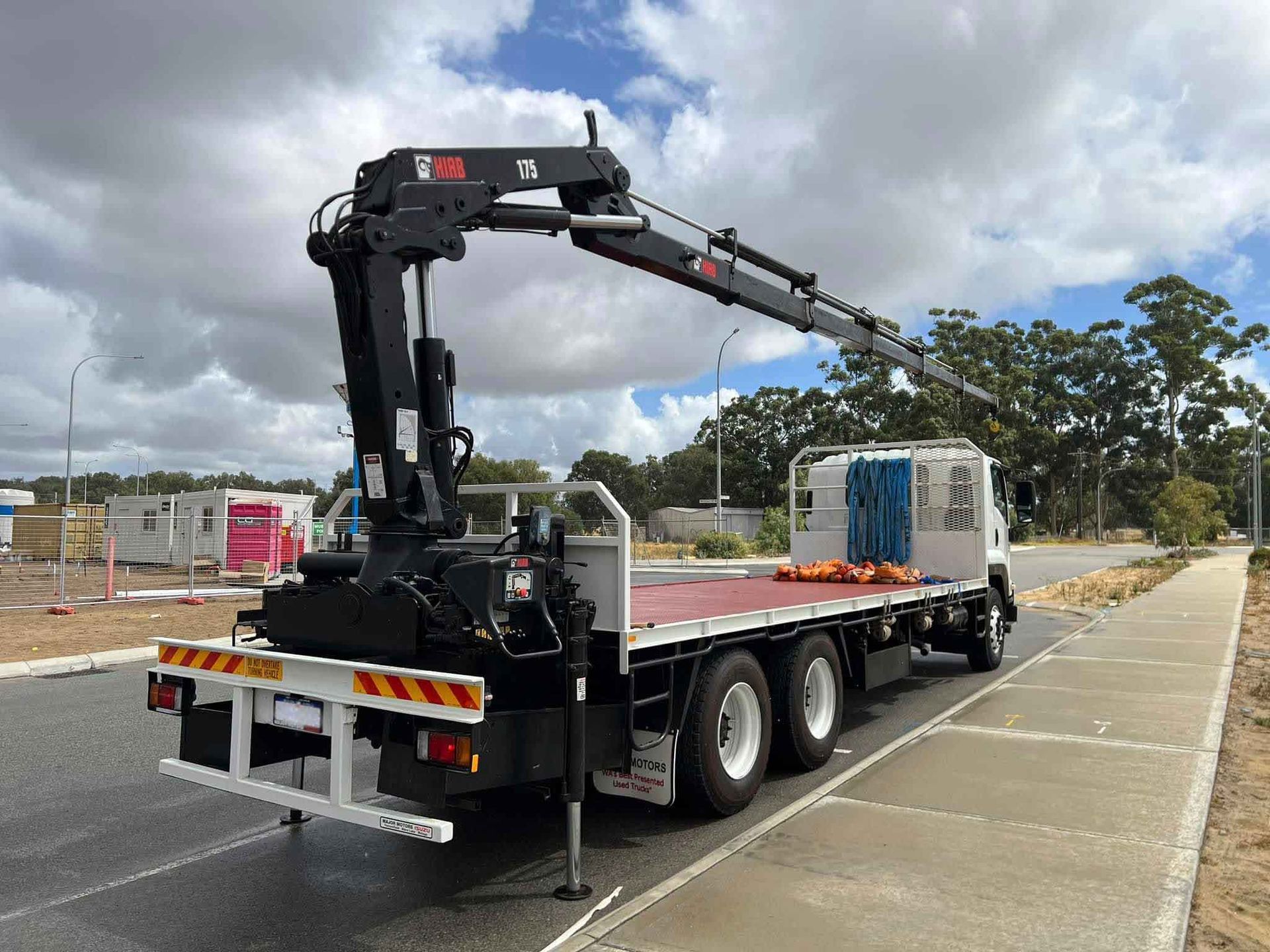 A flatbed truck with a crane on the back is parked on the side of the road.
