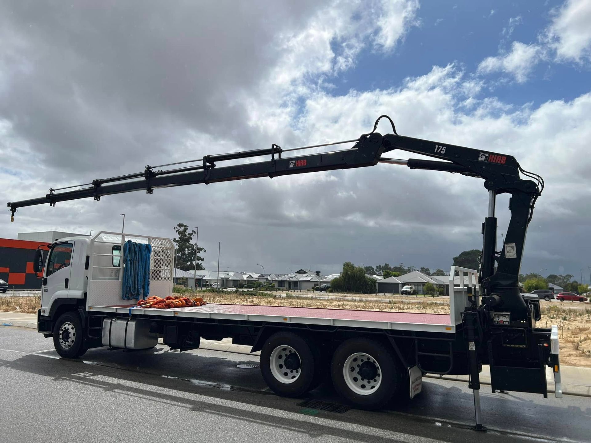 A flatbed truck with a crane attached to it is parked on the side of the road.