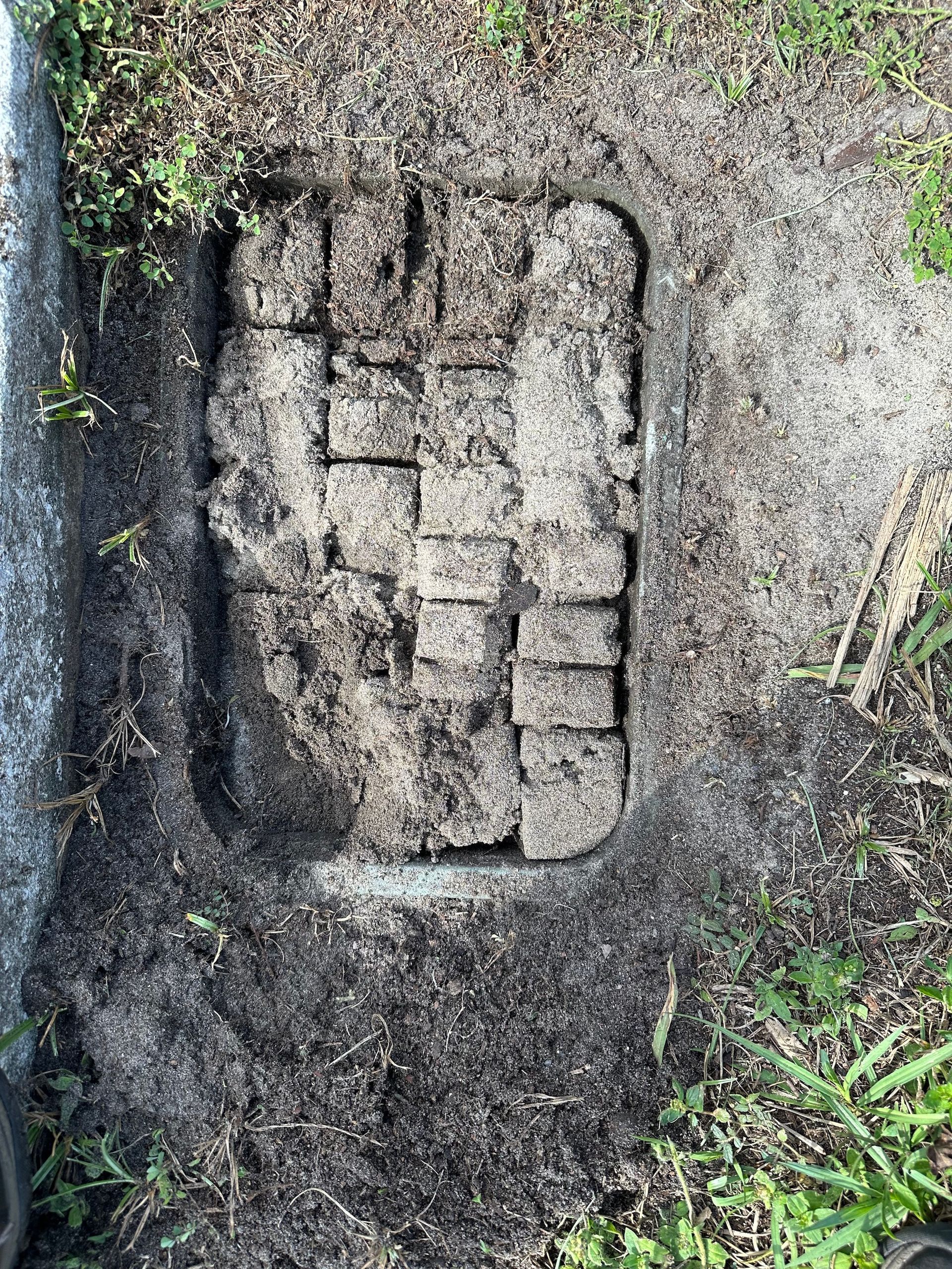 A brick wall is sitting in the dirt next to a stone wall.