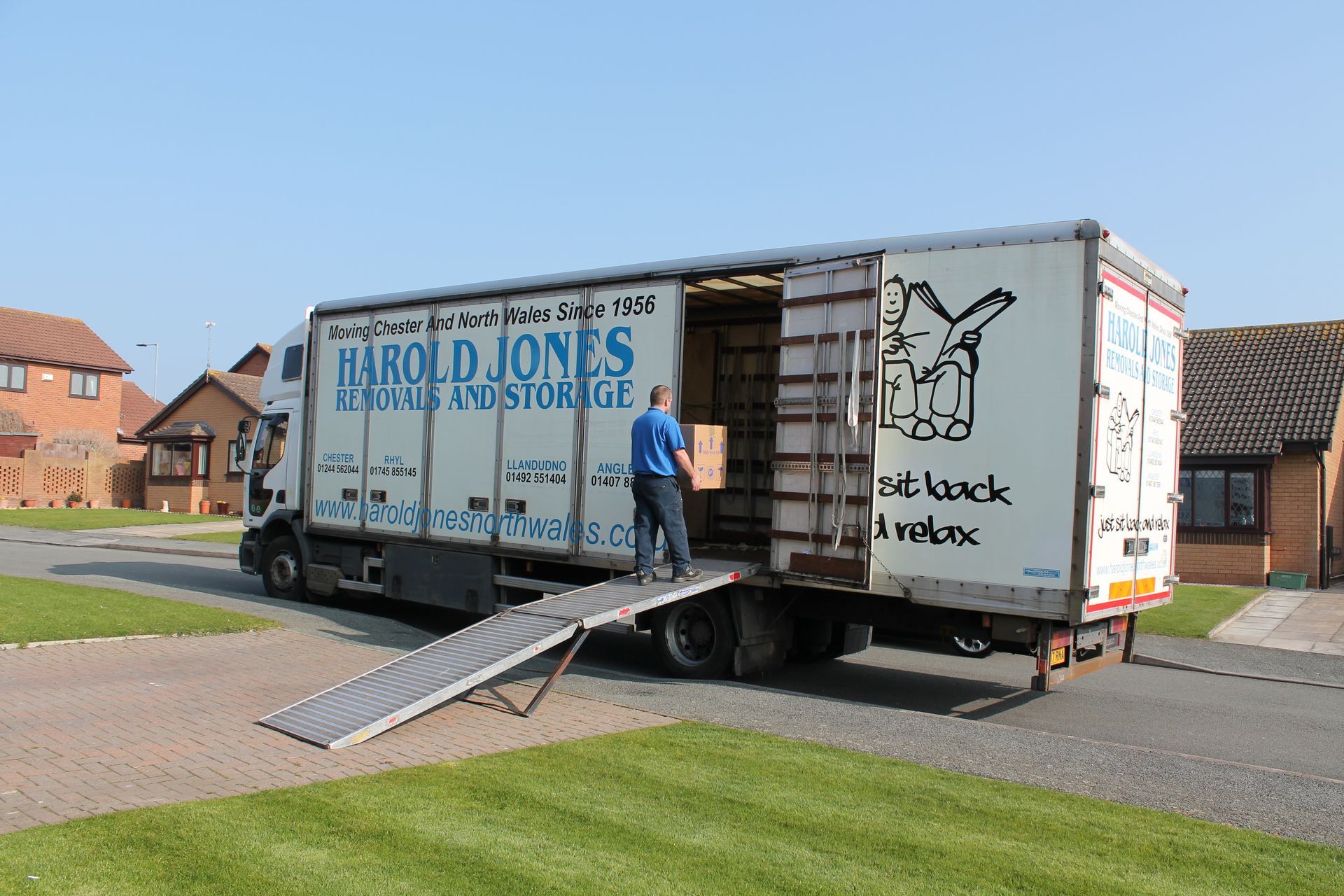 Harold Jones Removals & Storage truck with ramp parked on a North Wales street, with crew entering the open cargo area.