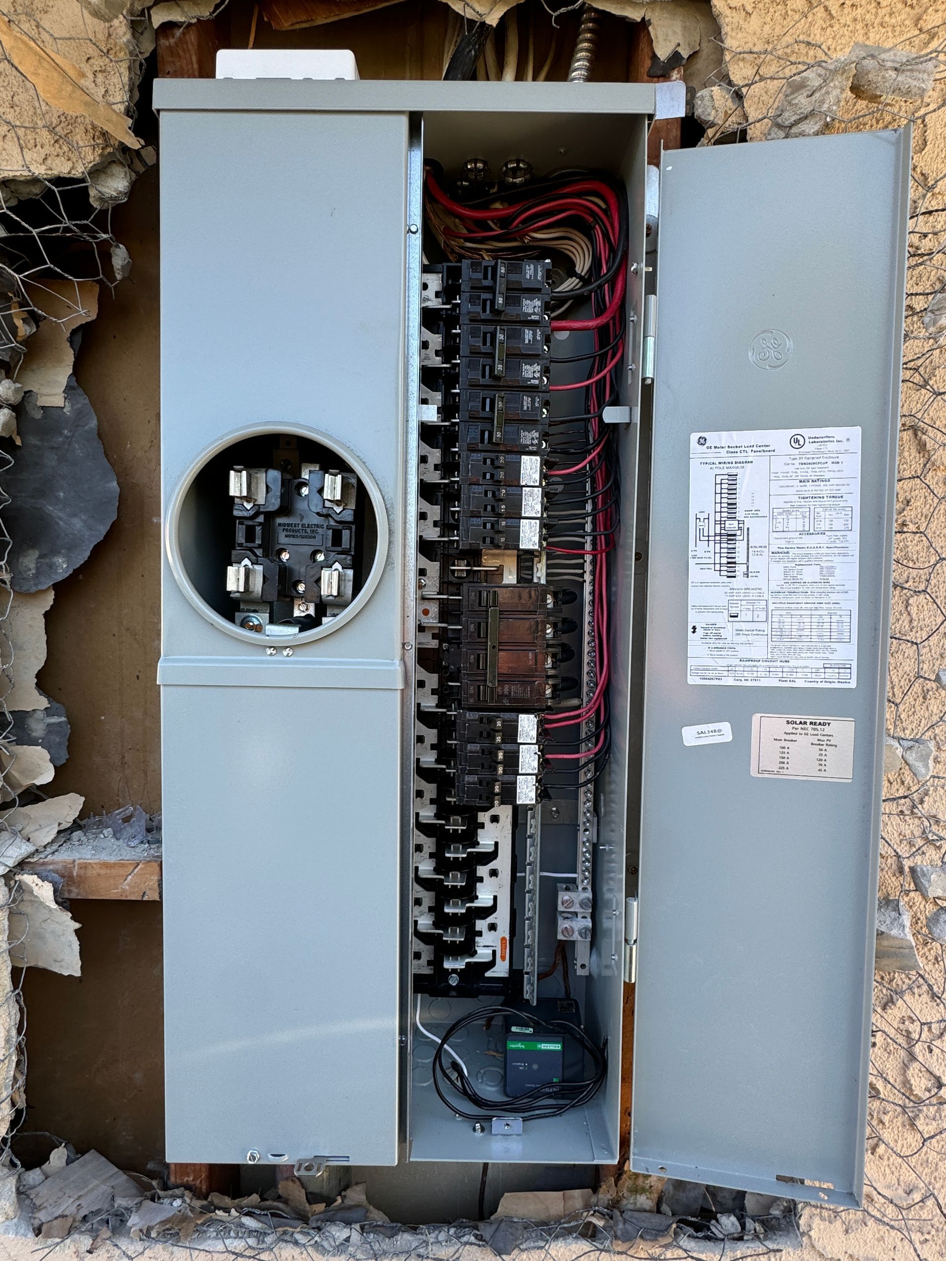 An electrical box is sitting in a hole in a wall.