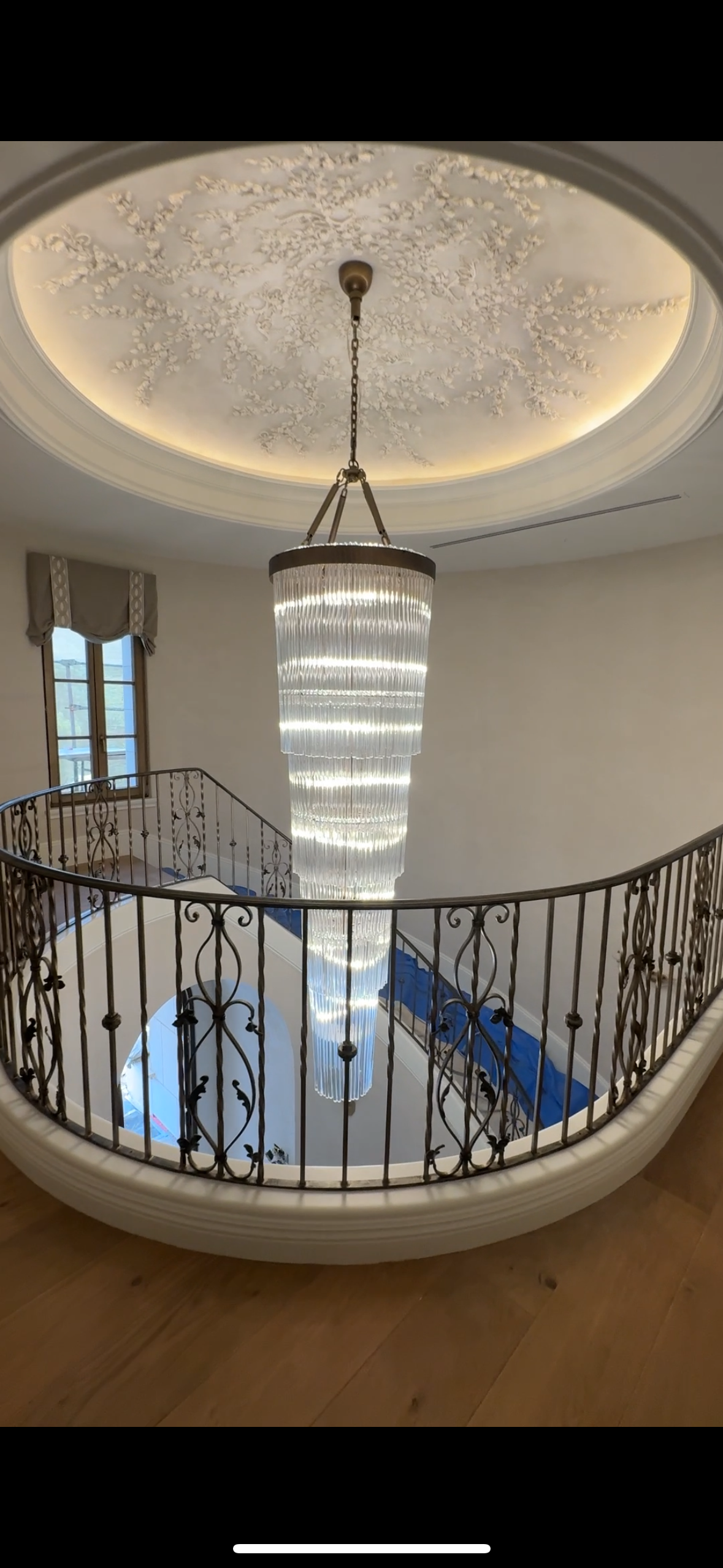 A large chandelier is hanging from the ceiling above a curved staircase.