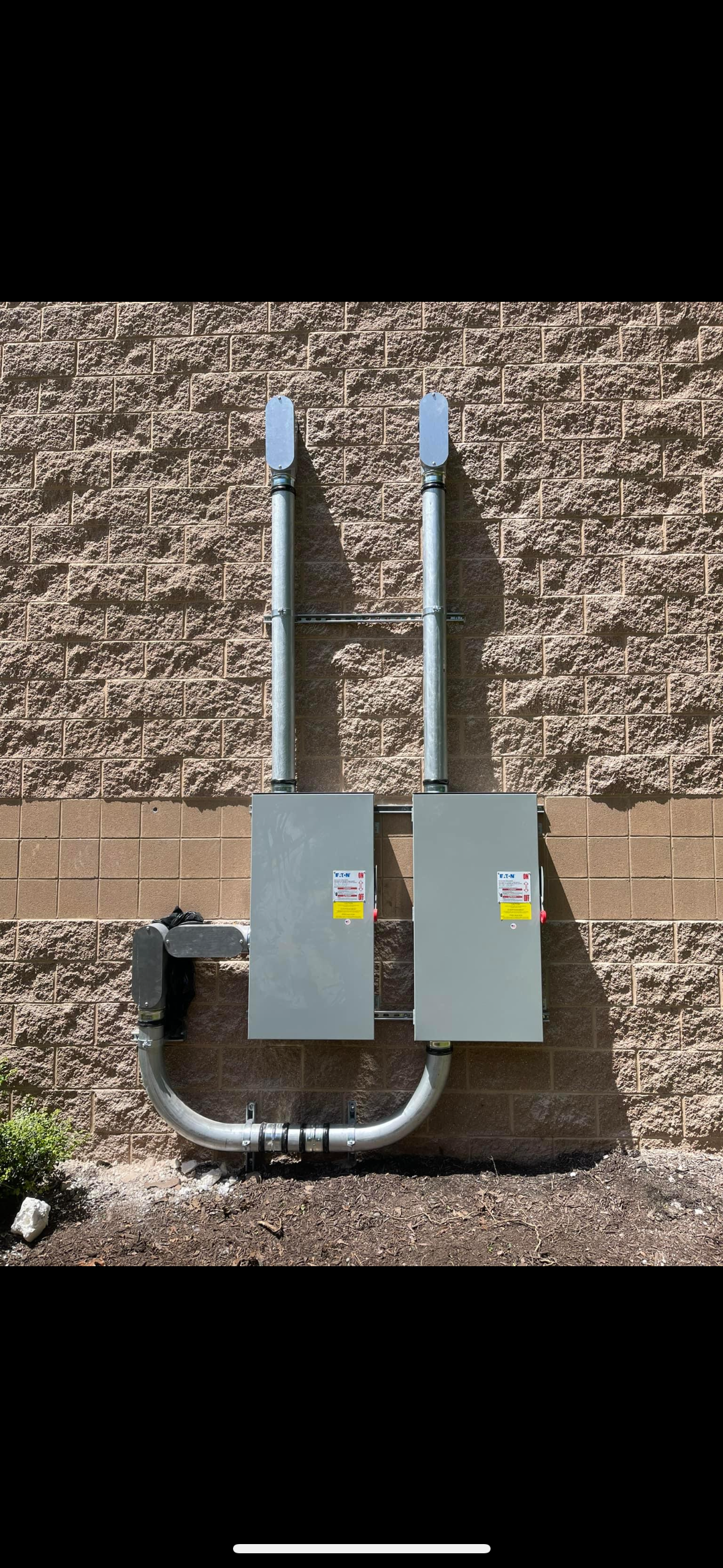 Two electrical boxes are attached to a brick wall.