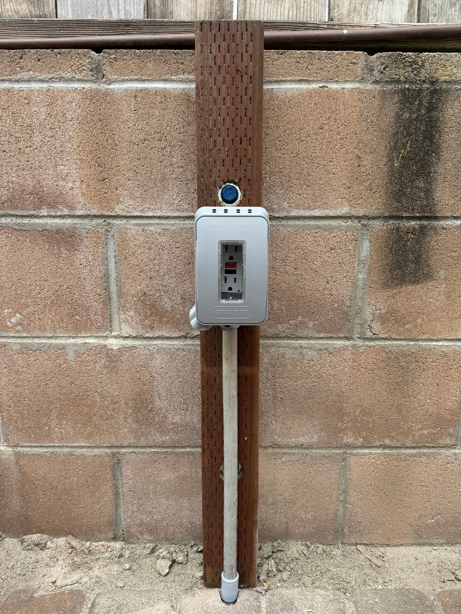 A brick wall with a wooden post and a metal box attached to it.