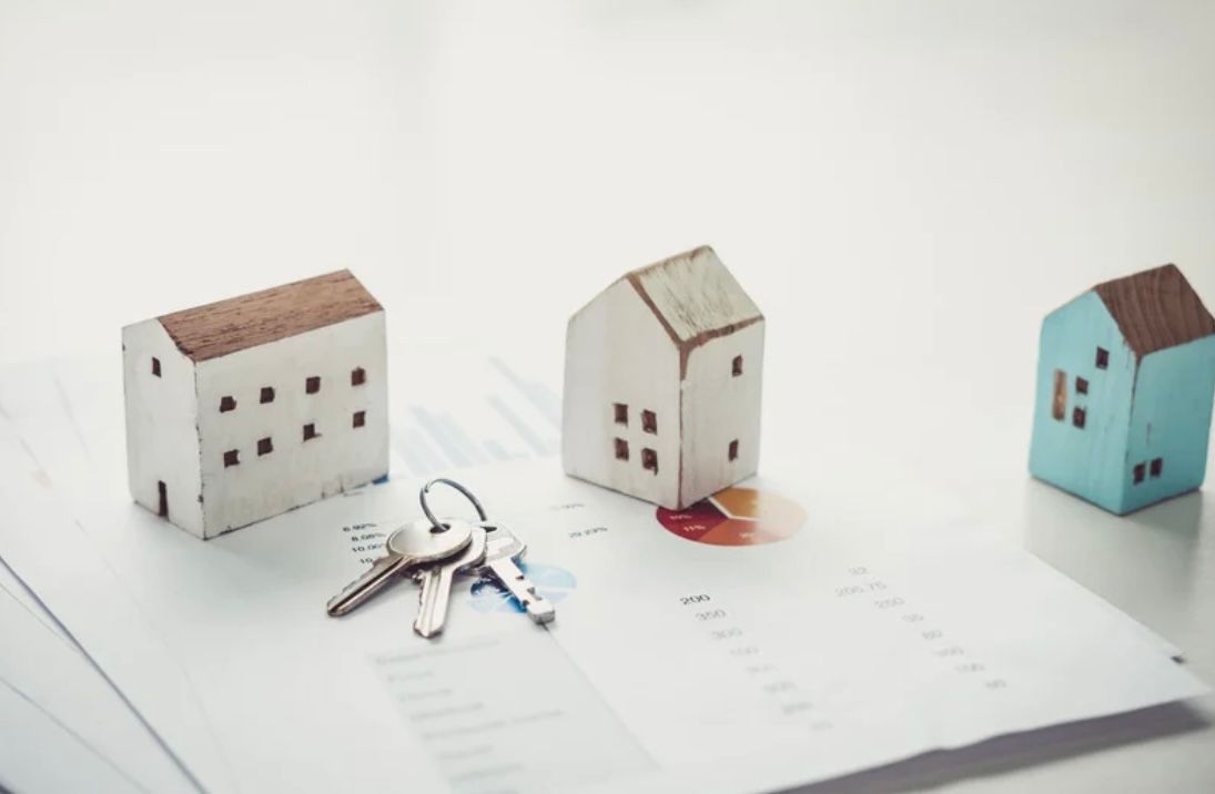 Casas en miniatura, llaves y documentos sobre una superficie blanca, simbolizando una transacción inmobiliaria.