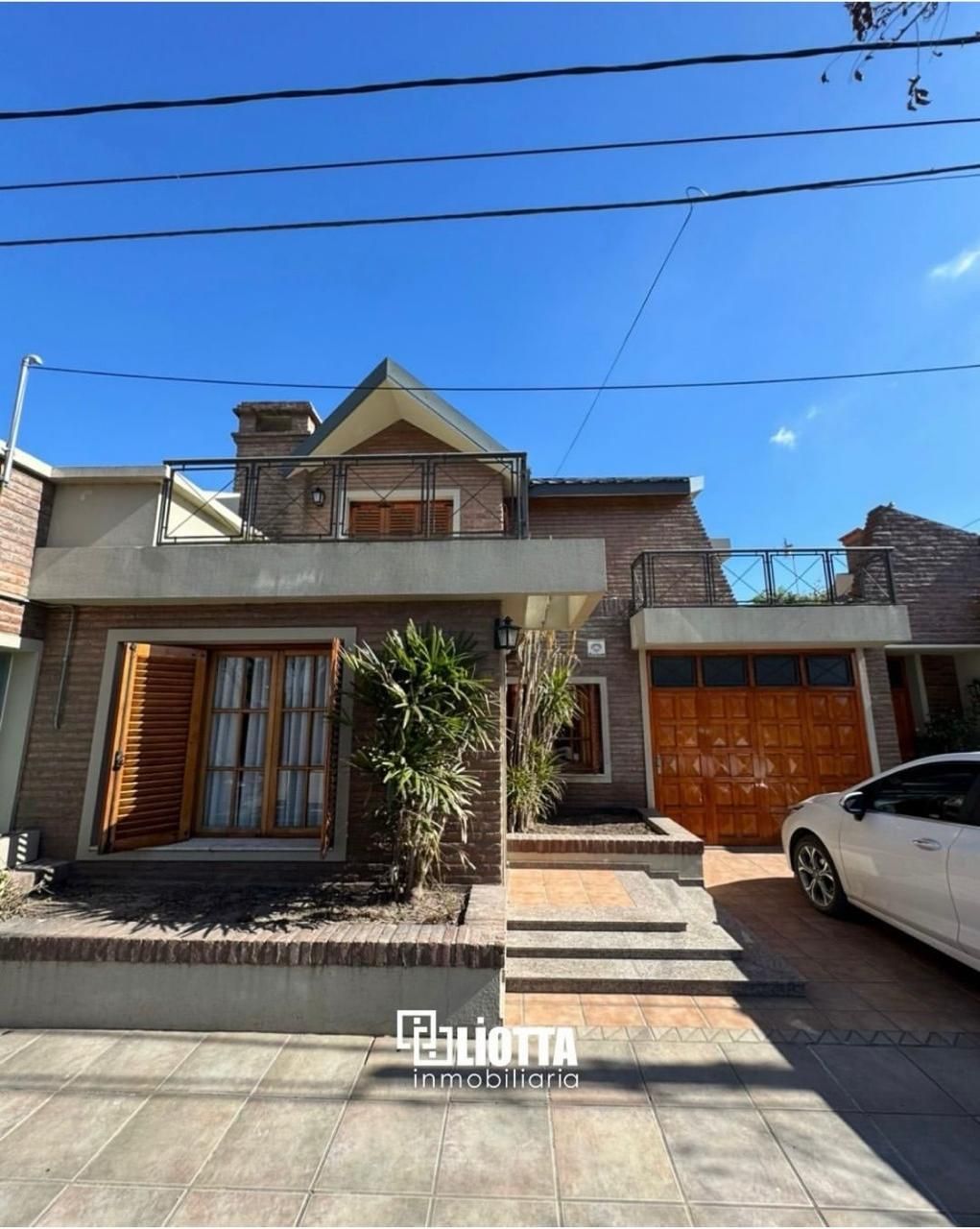 Exterior de casa con fachada de ladrillo, puerta de garaje de madera y un coche blanco aparcado delante.