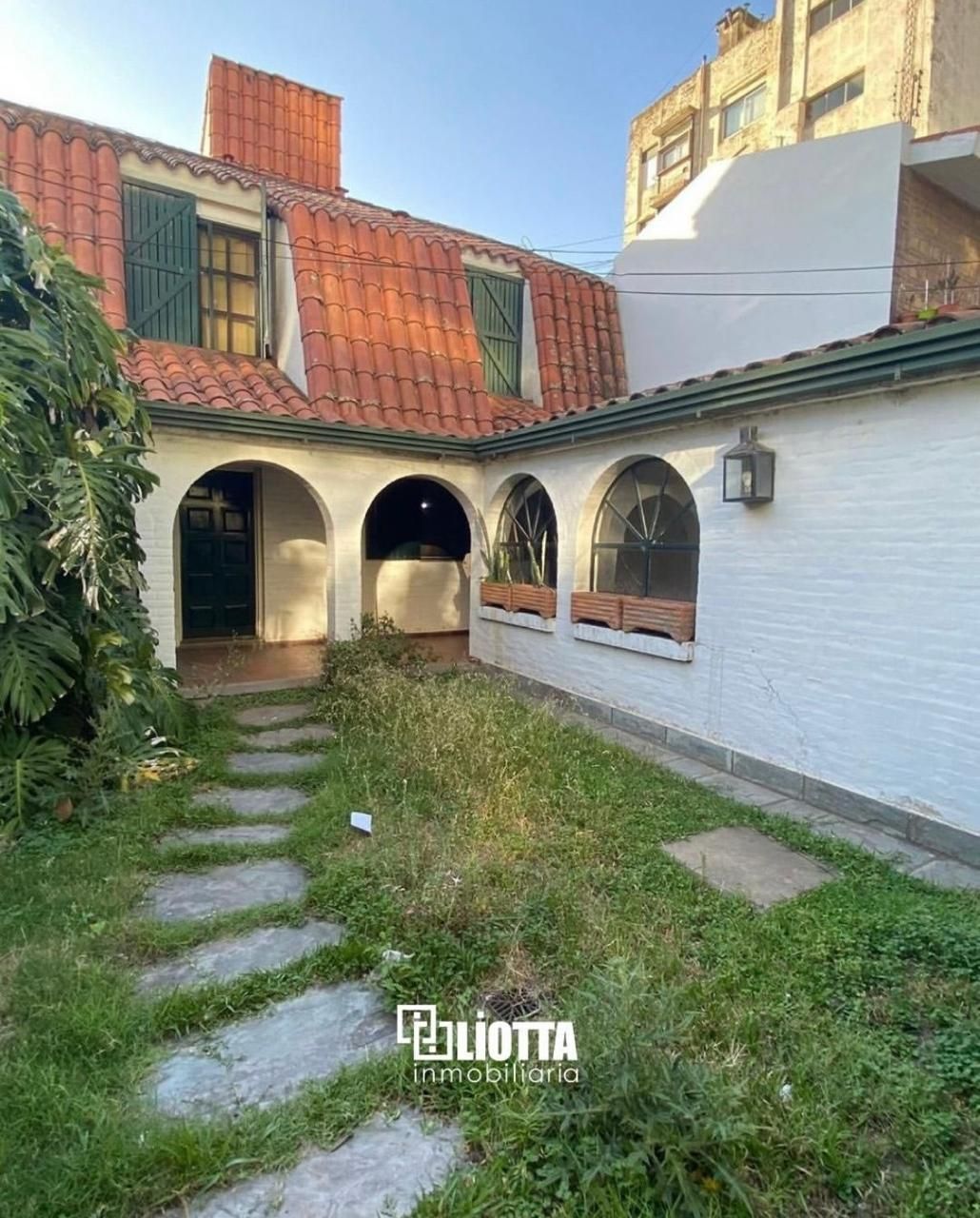 Edificio de paredes blancas con entrada arqueada y puerta de garaje verde en una calle de ladrillos.