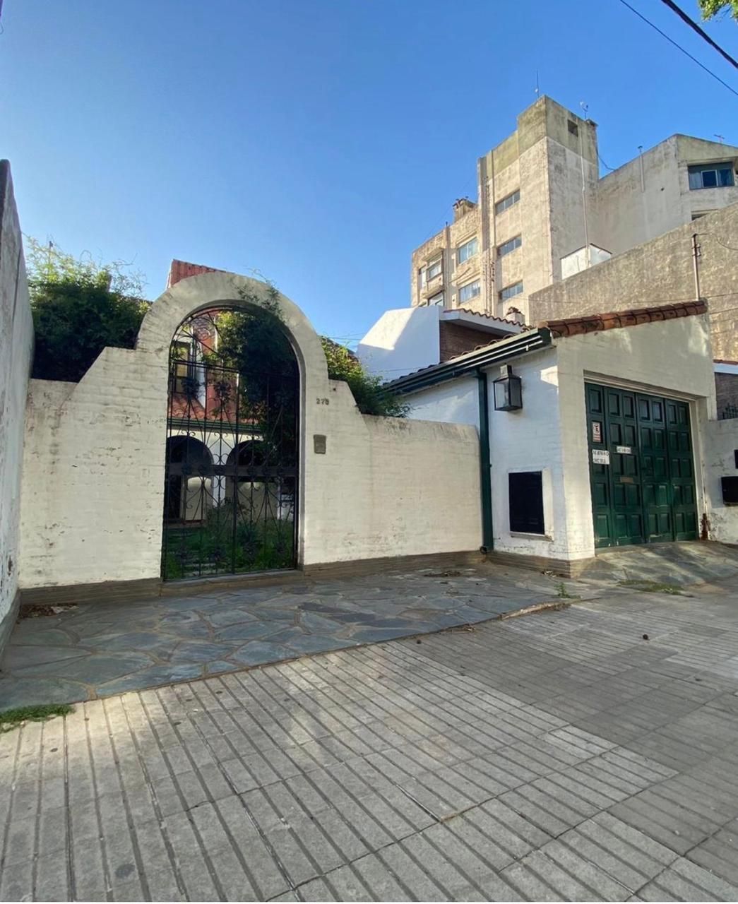 Edificio de paredes blancas con entrada arqueada y puerta de garaje verde en una calle de ladrillos.