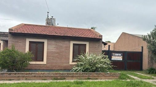 Casa de ladrillo con contraventanas marrones y techo de tejas rojas bajo un cielo nublado.