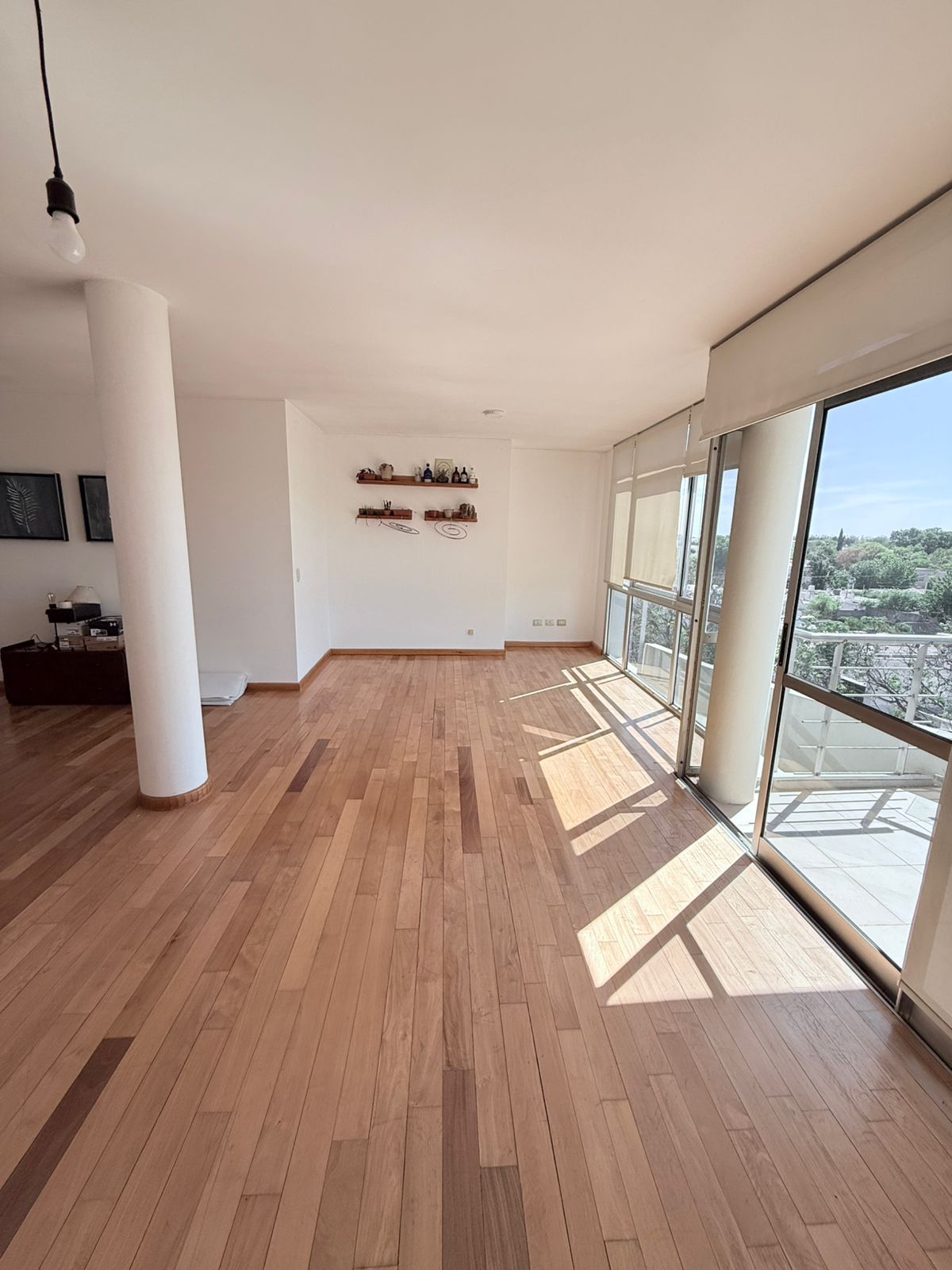 Habitación vacía con pisos de madera, ventanas grandes y un pilar central blanco.