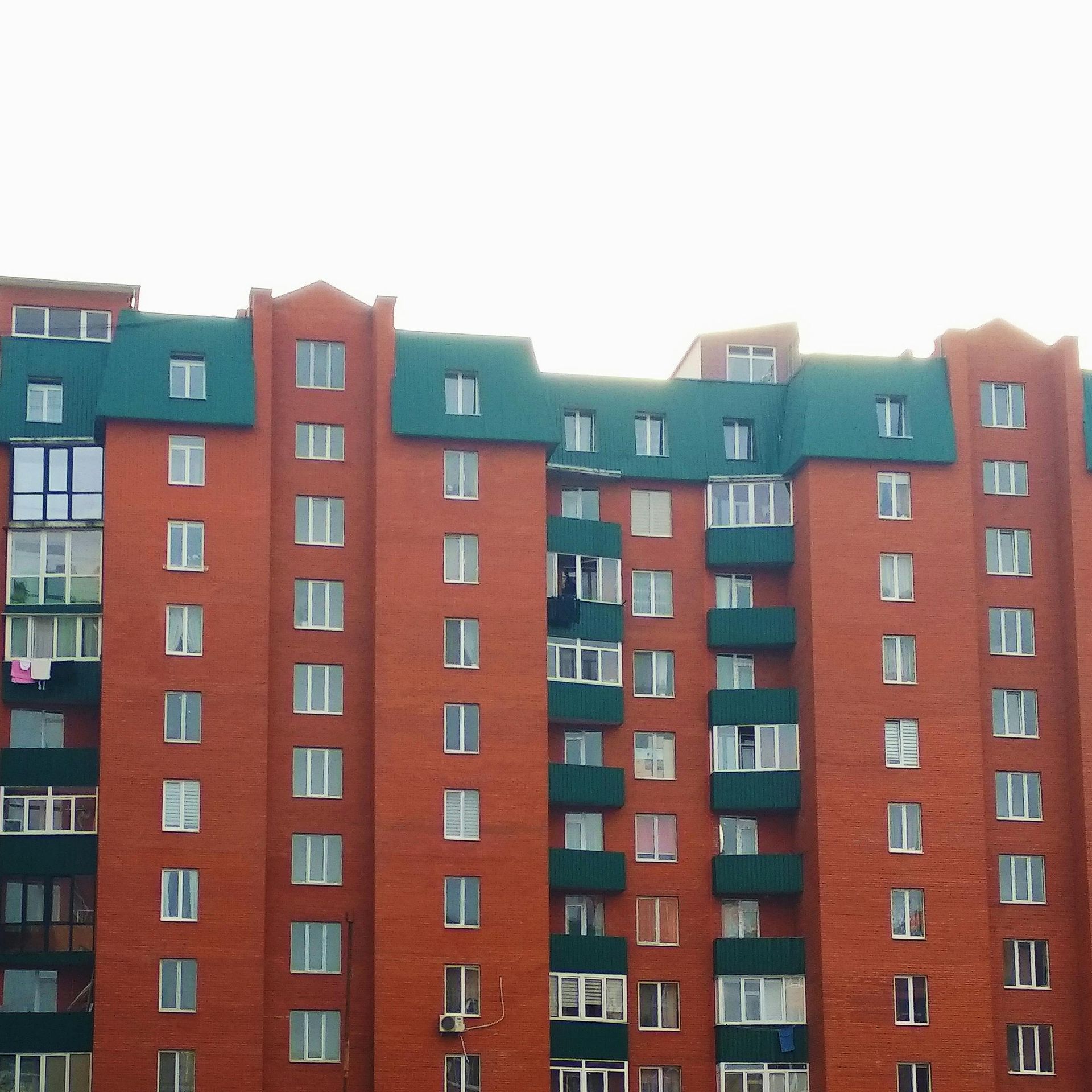 Edificio de apartamentos de ladrillo rojo con techo verde contra un cielo nublado.