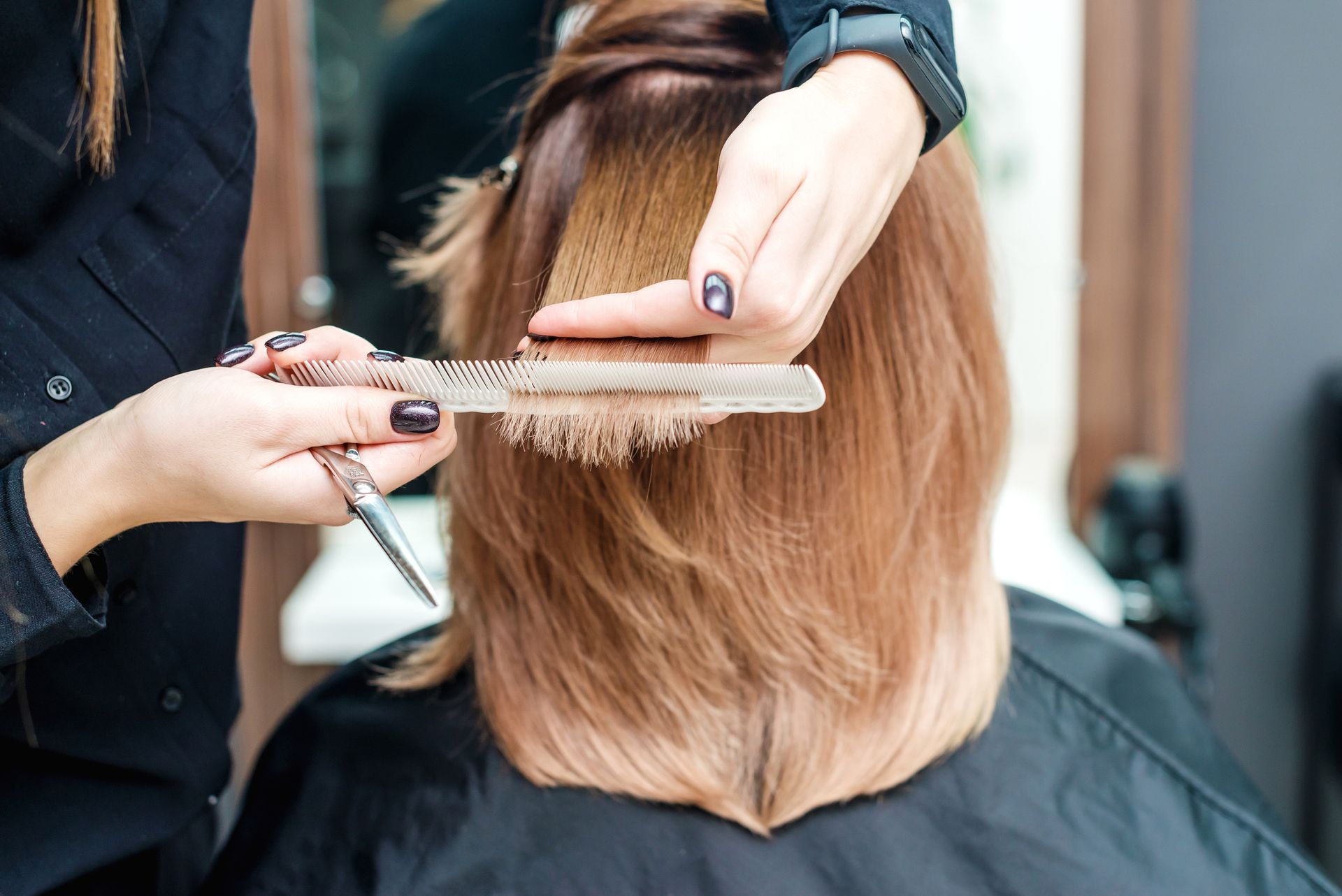 Hairdresser cutting a client's hair with scissors and comb in a salon. Hair is layered and dyed with a gradient effect.