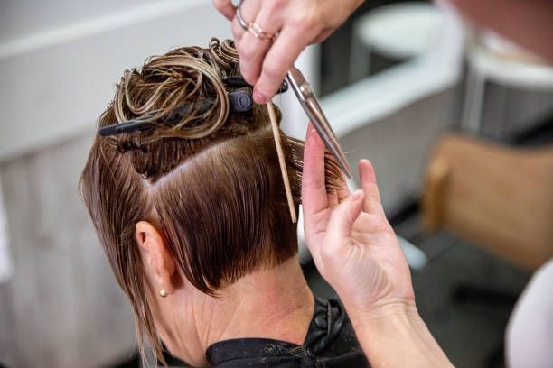 Hairdresser cutting a client's hair with scissors and a comb. Focus on the nape, hair is partially up and parted.
