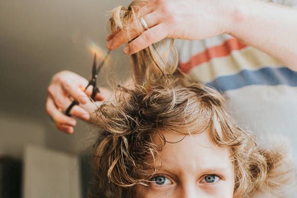 Person getting a haircut; scissors cutting blonde wavy hair. Blue eyes look toward the camera.