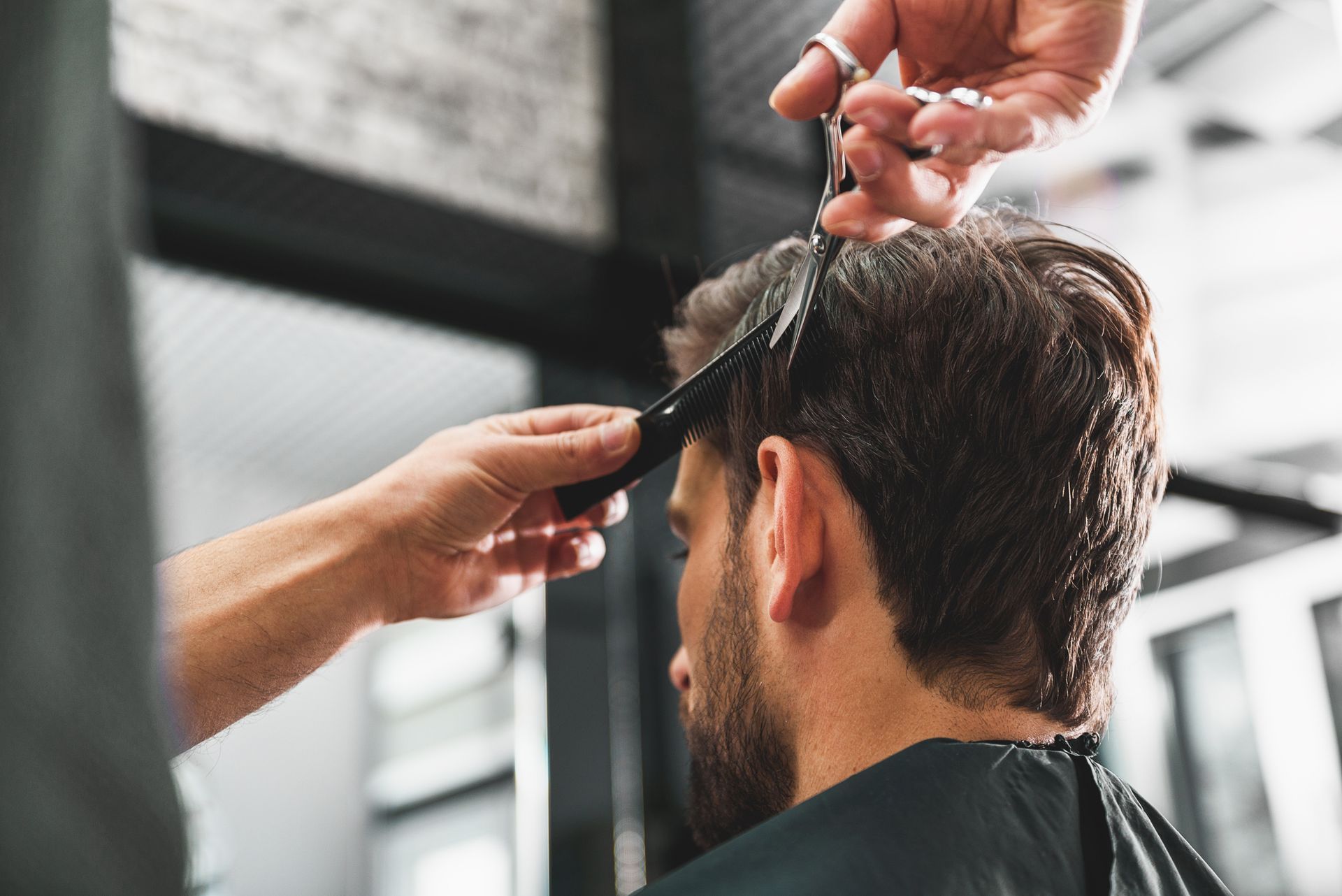 A person getting a haircut. A hand holds a comb and scissors close to the client's hair in a salon.