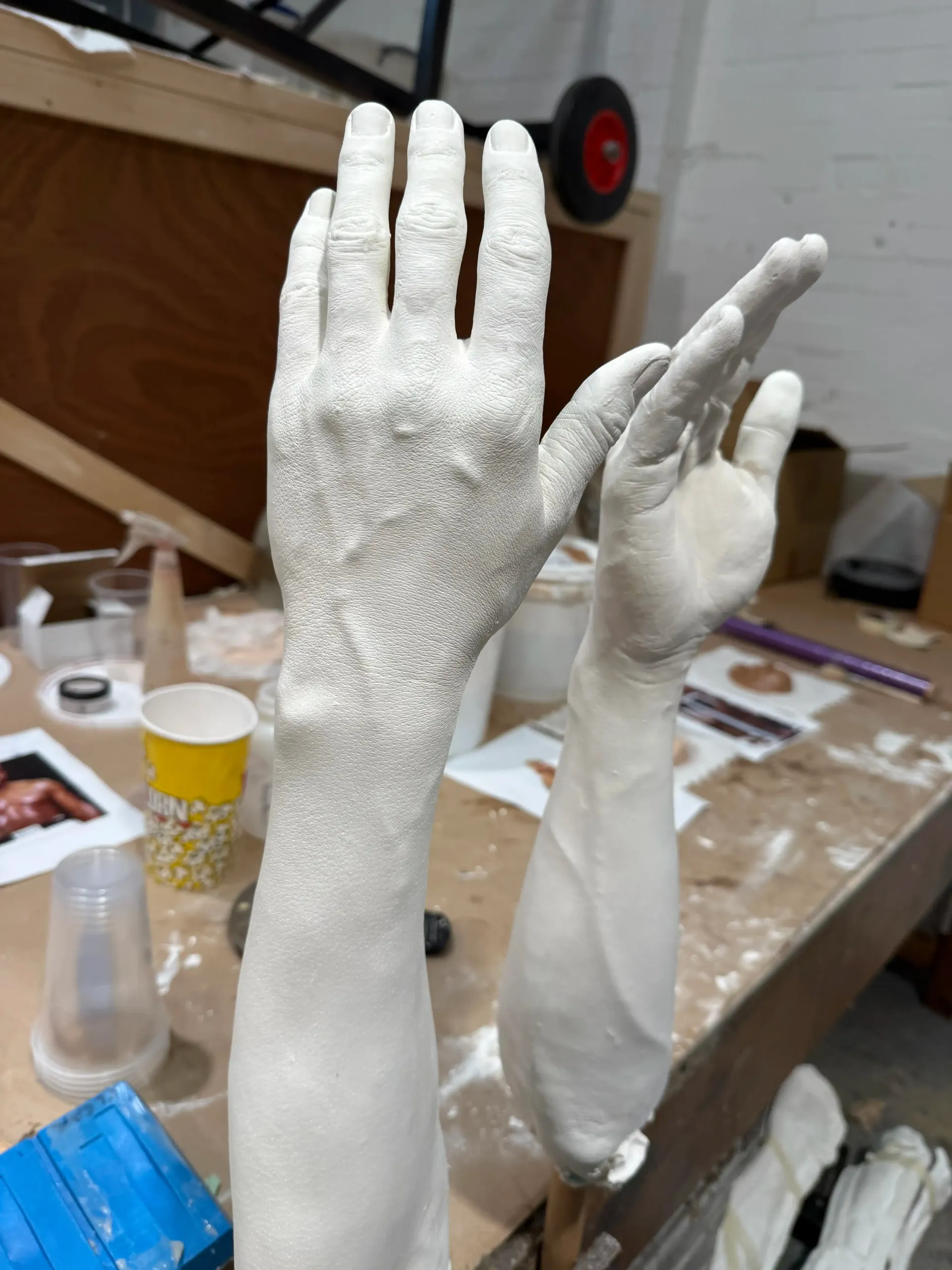 Two white plaster hands with arms, one covered in texture, on a workbench.
