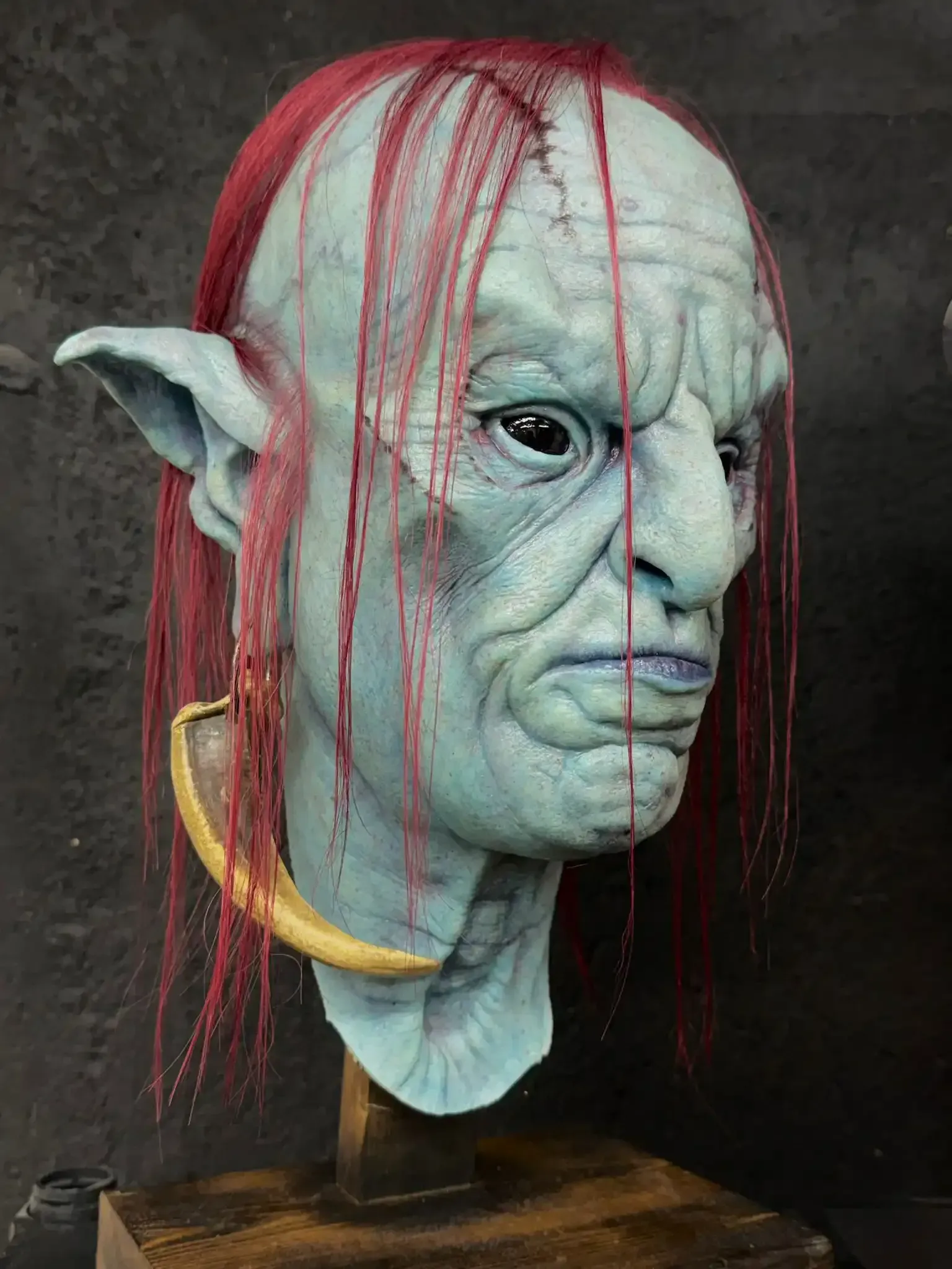 Zombie mask with exposed flesh and skull-like features, brown hair, displayed on a stand.