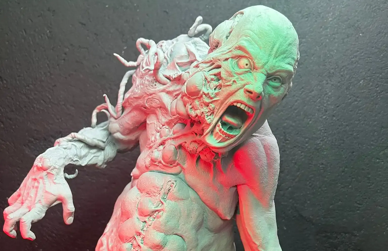 A sculpture of a monstrous, mutated figure with a distorted face screaming, textured flesh, and tentacle-like protrusions.