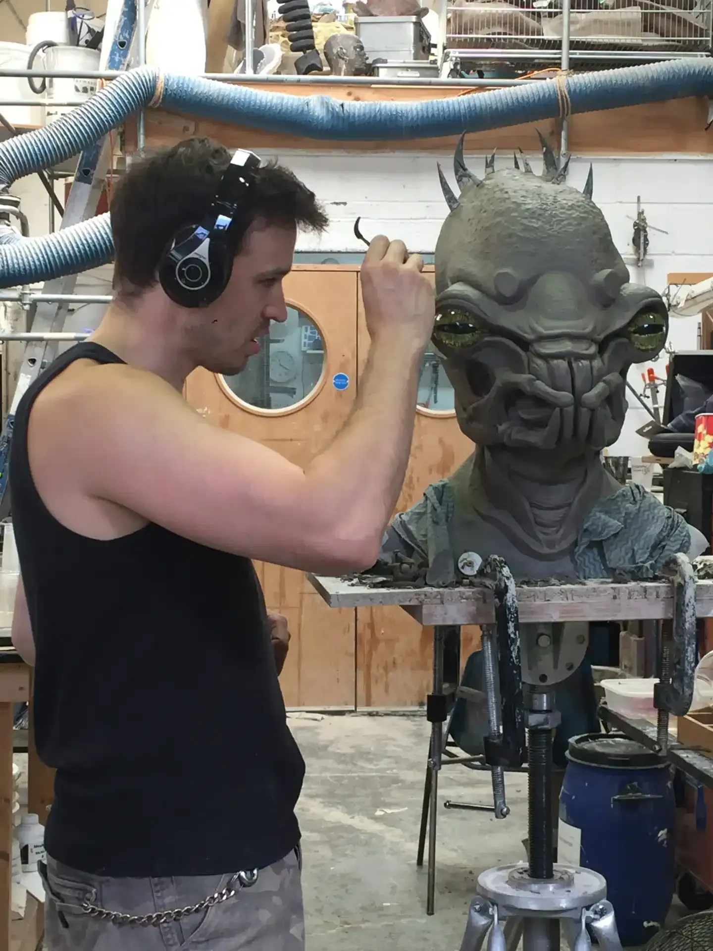 Man carving a creature sculpture, wearing ear protection, in a workshop.