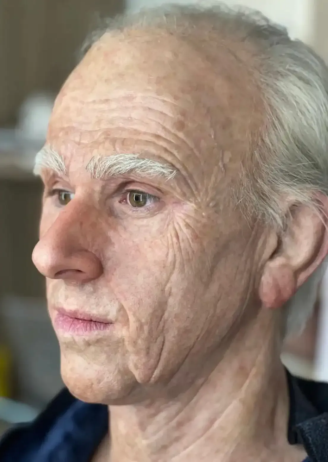 Close-up of a person with fair skin, grey hair, and wrinkles, likely older.