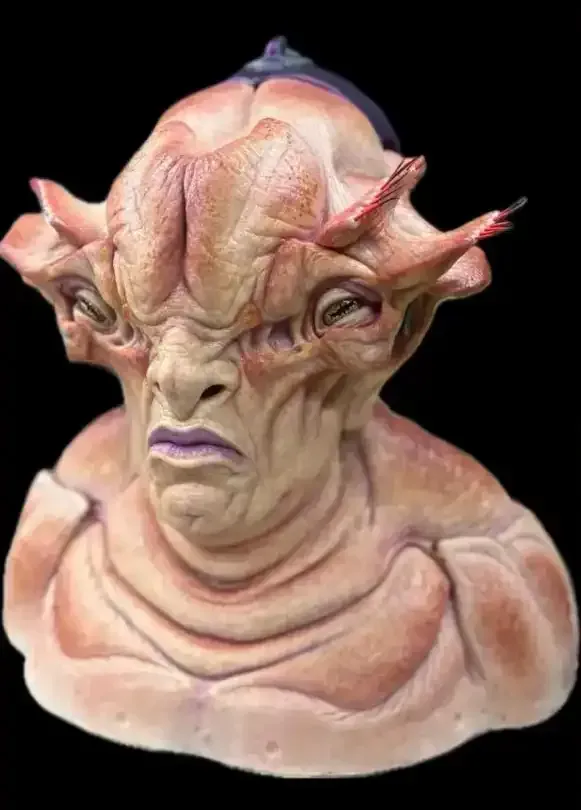 Alien bust with pink skin, stern expression, and multiple appendages around the head.