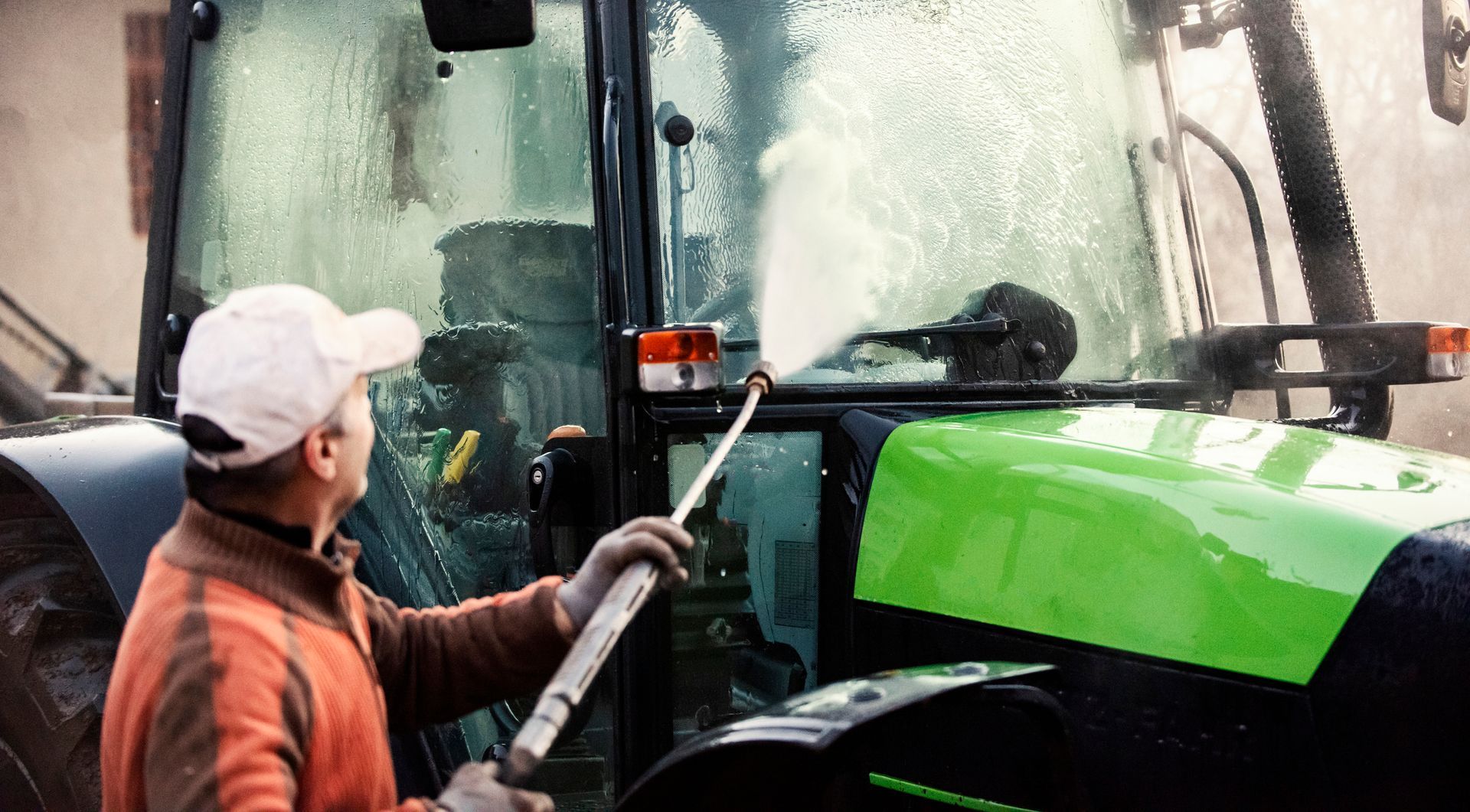 A man is washing a green tractor with a high pressure washer