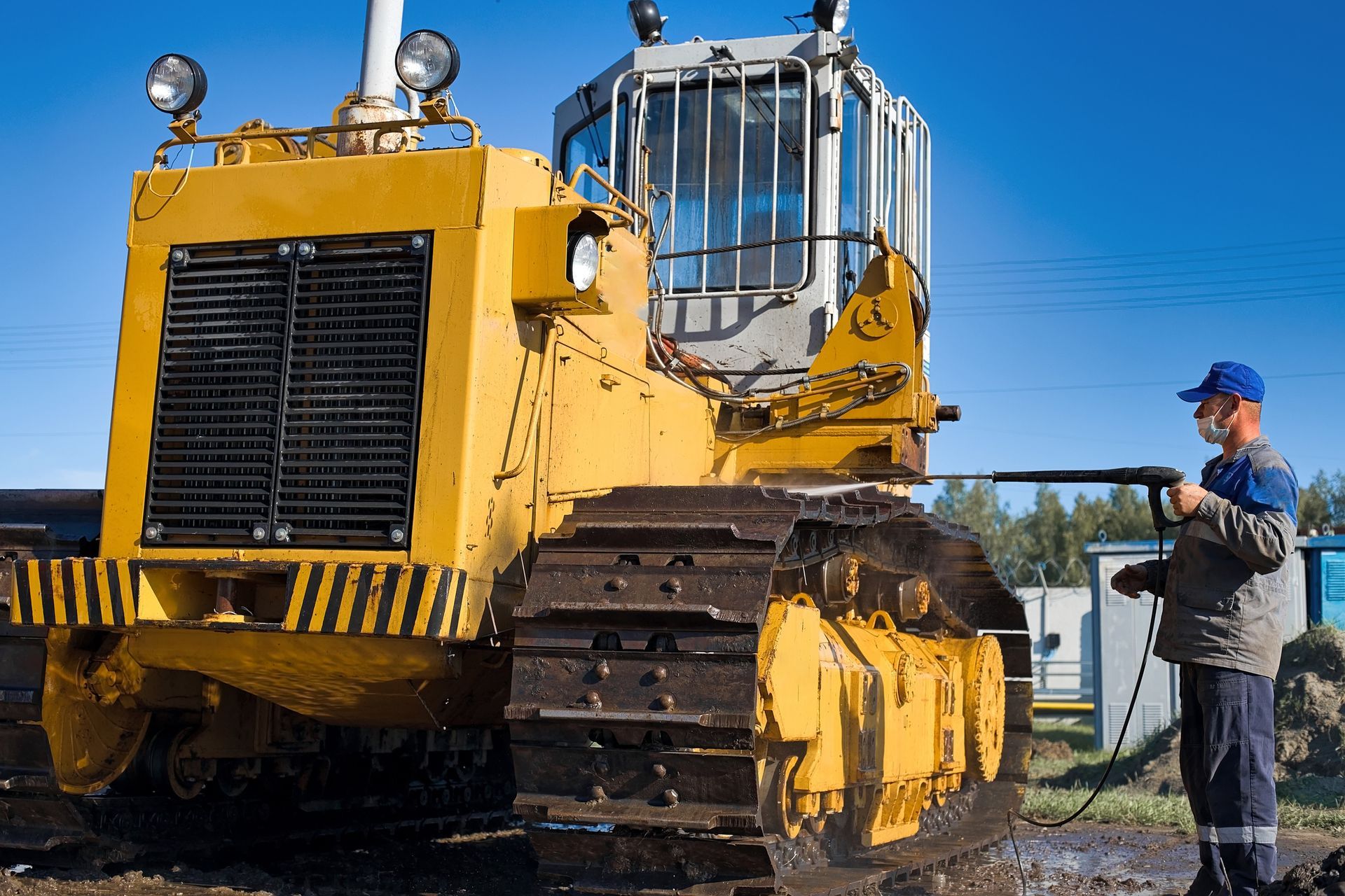 A man is cleaning a yellow bulldozer with a high pressure washer.