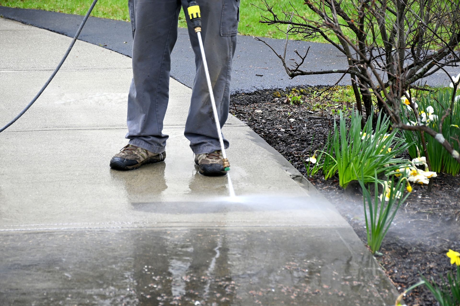 A man is using a high pressure washer to clean a sidewalk