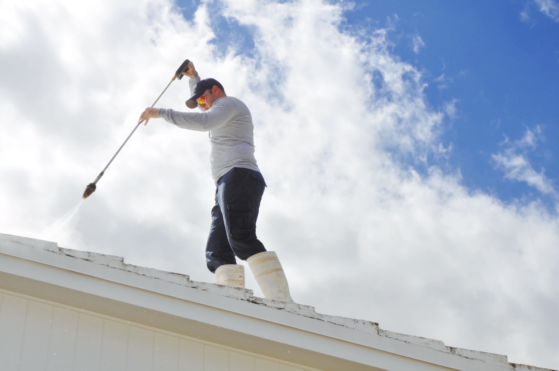 A man is cleaning the roof of a house with a high pressure washer.