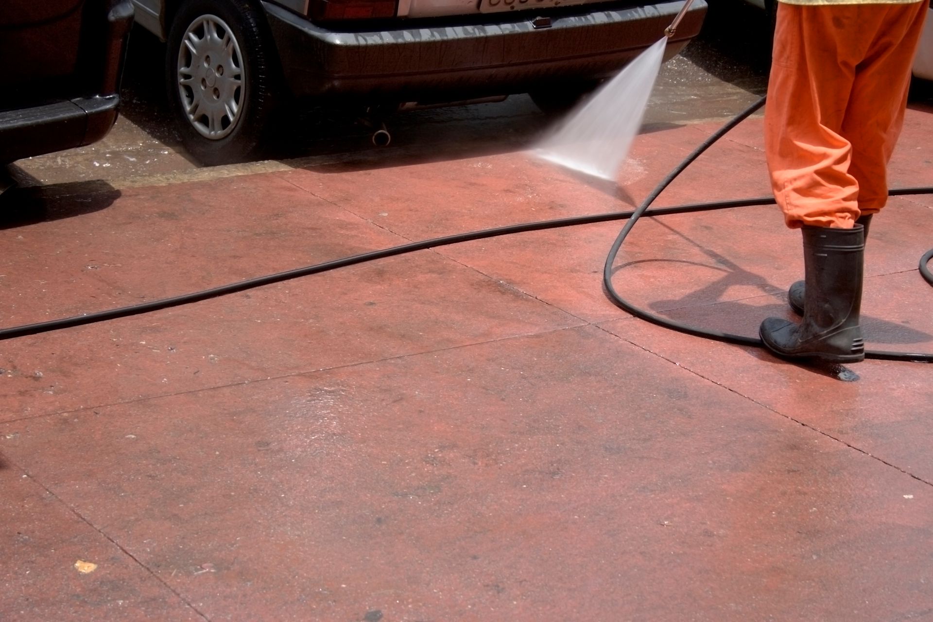 A man in orange pants is using a high pressure hose to clean a driveway