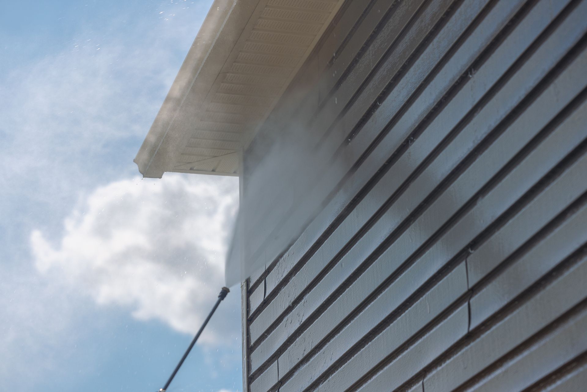 A person is cleaning the side of a house with a high pressure washer.