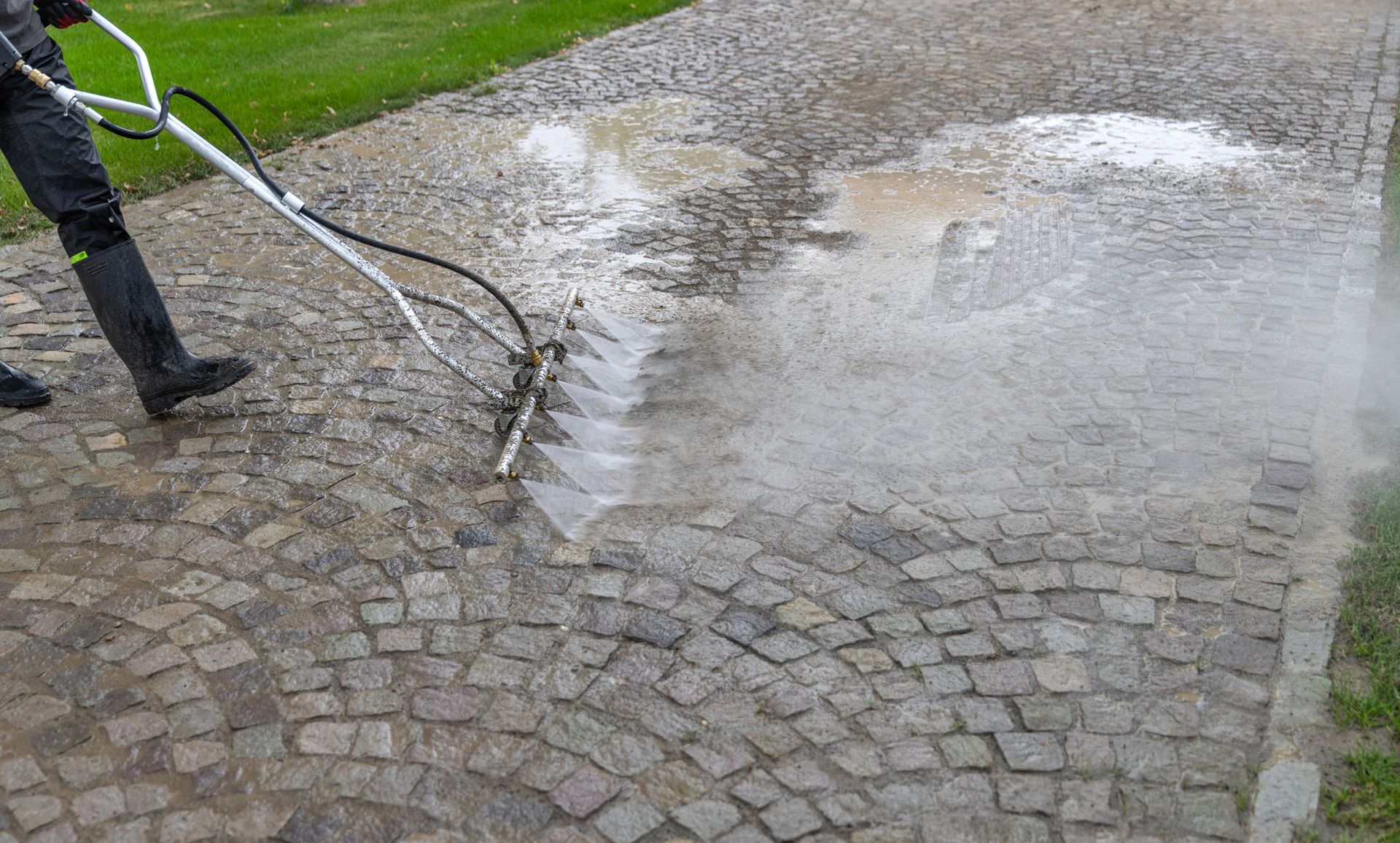 A man is using a high pressure washer to clean a cobblestone driveway.